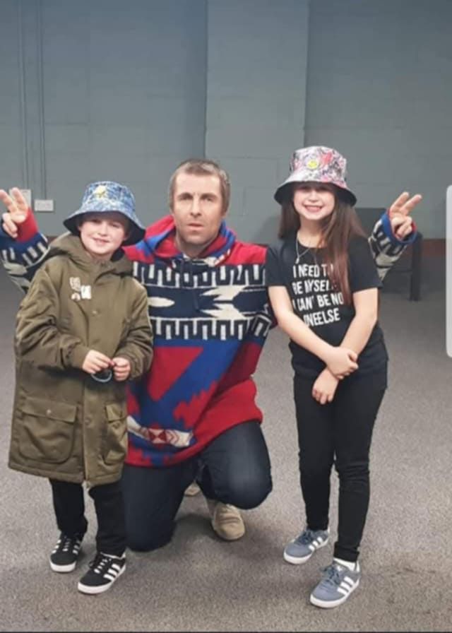 Liam Gallagher posing with two young fans backstage