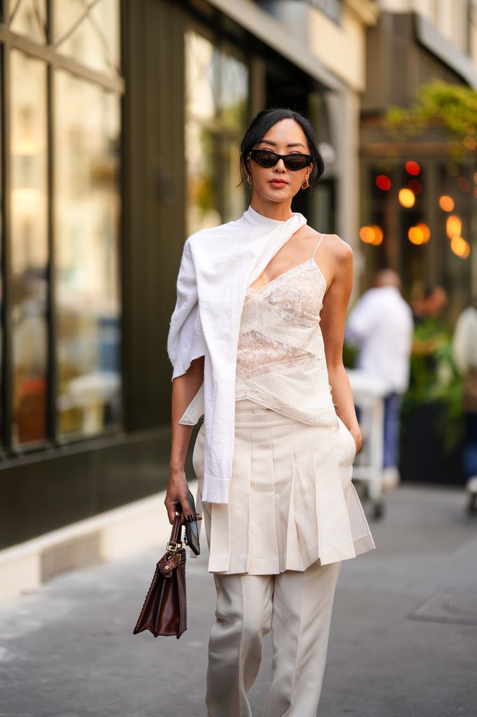 Chriselle Lim wears black sunglasses from Fendi, gold embossed cut-out logo earrings from Fendi, a white wool scarf, a white embossed lace pattern V-neck / backless / silk tank-top, white latte wide legs suit pants with embroidered pleated / accordion short skirt belt from Fendi, a dark brown shiny leather Peekaboo handbag from Fendi,
