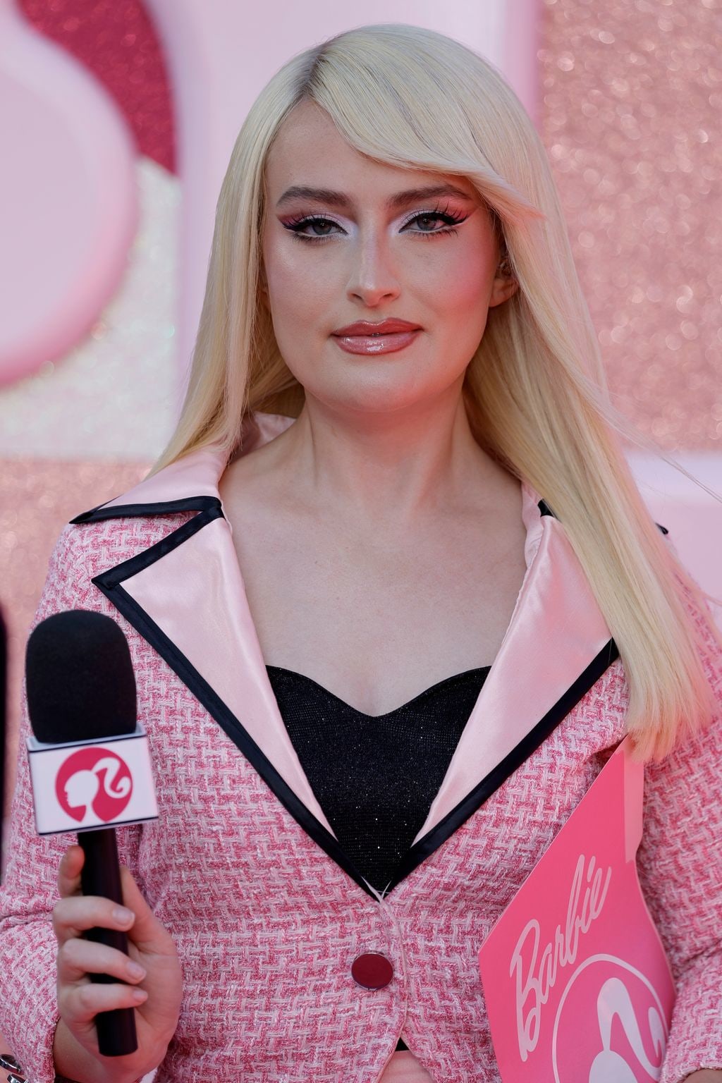 Amelia Dimoldenberg wears a pink suit and holds a Barbie-themed microphone