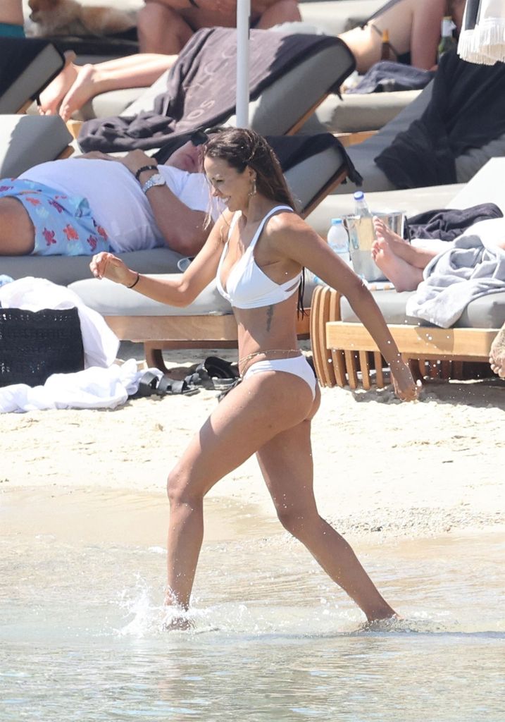 Luciana Barroso strides through the water's edge on a beach in Greece