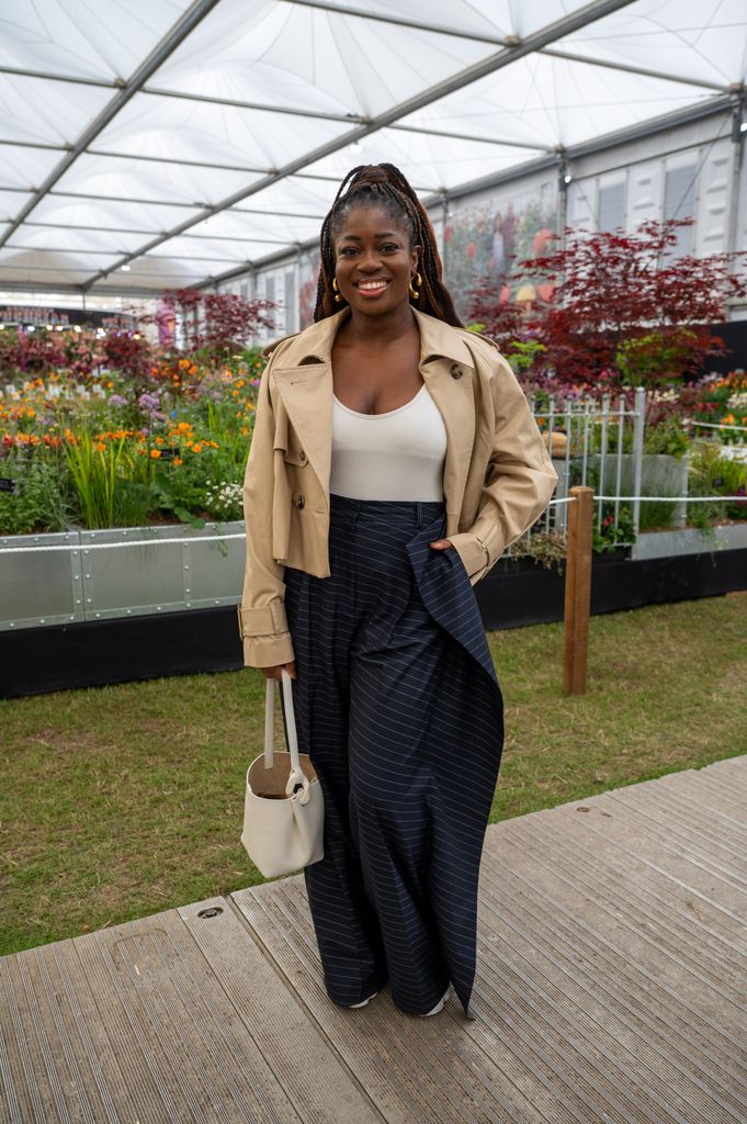 Clara Amfo at Chelsea Flower Show in pinstriped wide-leg trousers, beige cropped trench coat, and white bodysuit carrying a structured cream handbag.