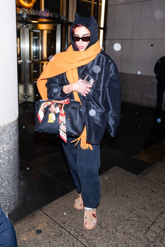 Dua Lipa is spotted in NYC wearing UGG slippers, trackpants, an orange scarf, sunglasses and a Birkin bag
