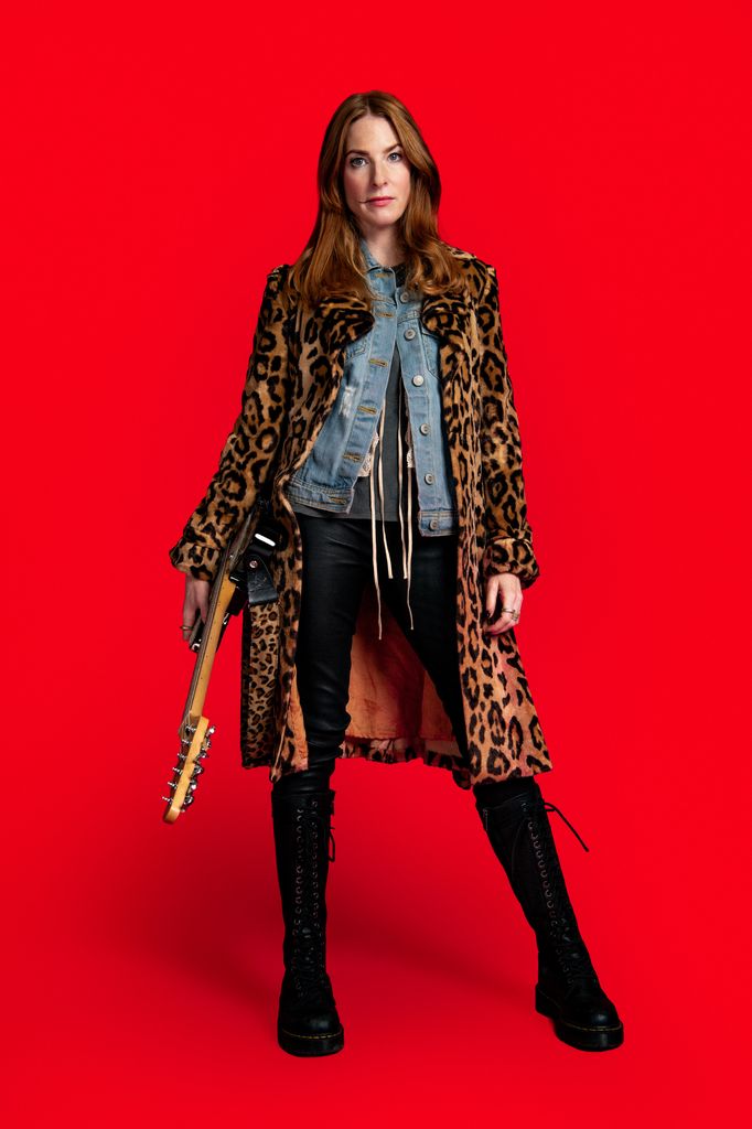 Actress Rosalie Craig in a leopard print jacket with a guitar on a red background