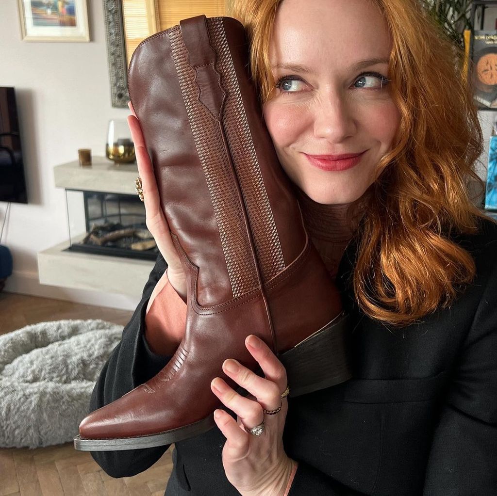 Christina Hendricks holds up a cowboy boot to the side of her face