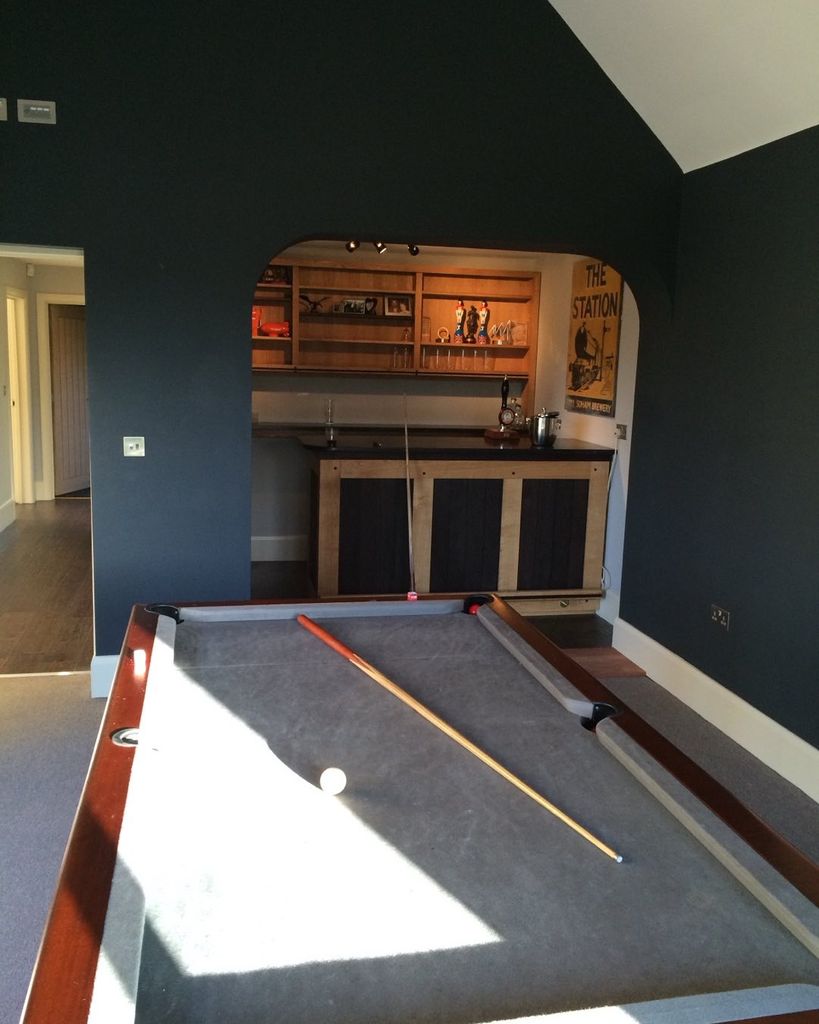 A pool table and small bar in a navy blue room