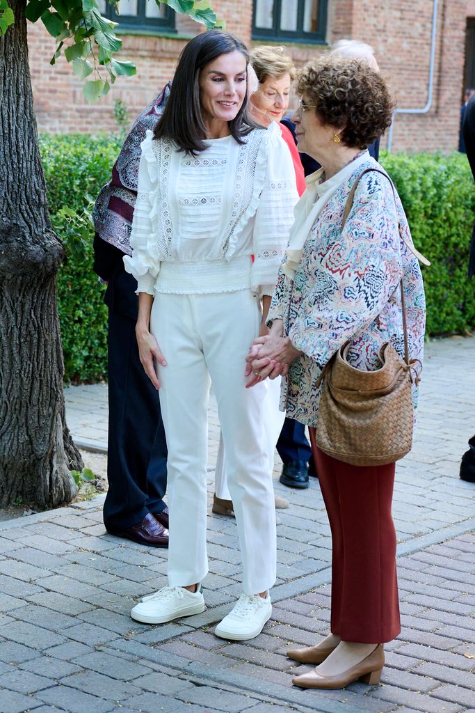 Queen Letizia in white blouse and trousers talking to a lady