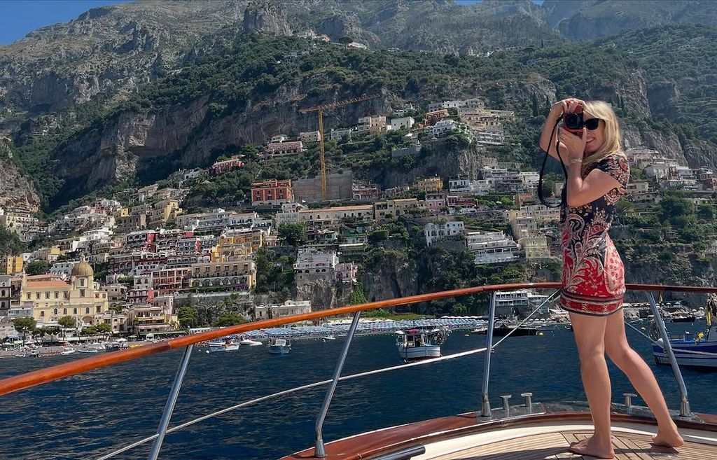 Sam Taylor Johnson standing on a boat holding a camera in front of Positano while on holiday