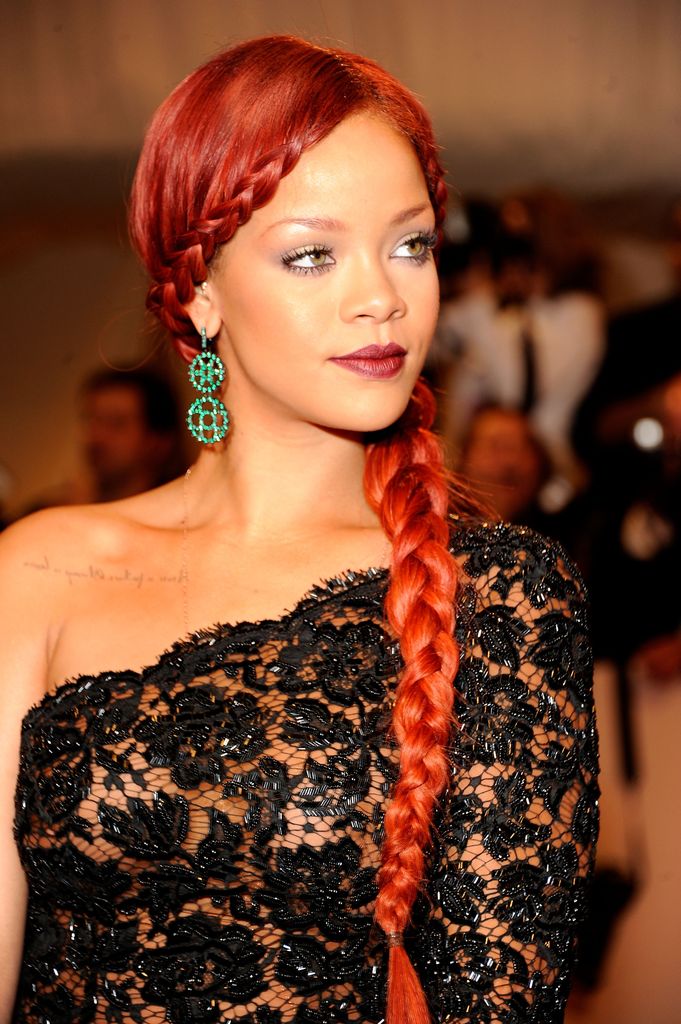 Rihanna at the 2011 Met Gala in emerald chandelier earrings, red braid, and a black lace gown.