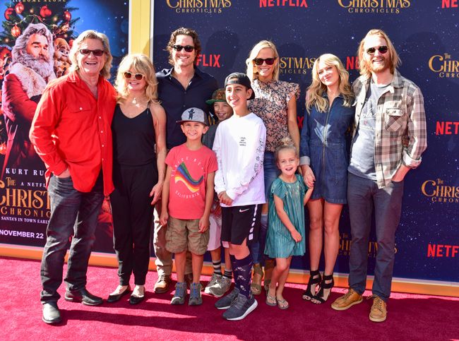 a family of six adults and four children gathered and standing casually dressed in the bright sunshine on a red carpet and they are smiling