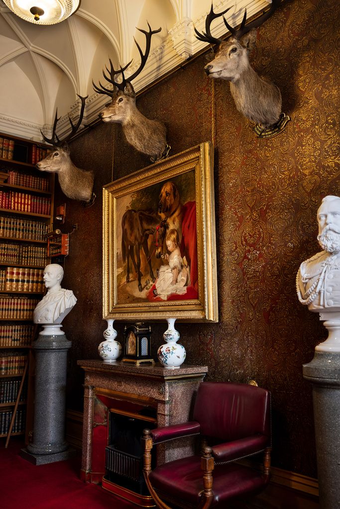 A room with a painting, bookshelves and three mounted deer heads