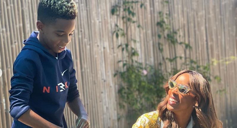 A young boy stood with Kelly Rowland in a garden