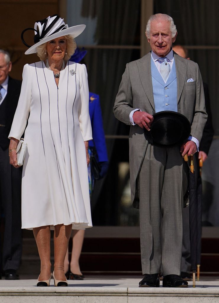 Rainha Camilla em vestido preto e branco e chapéu com o Rei Charles