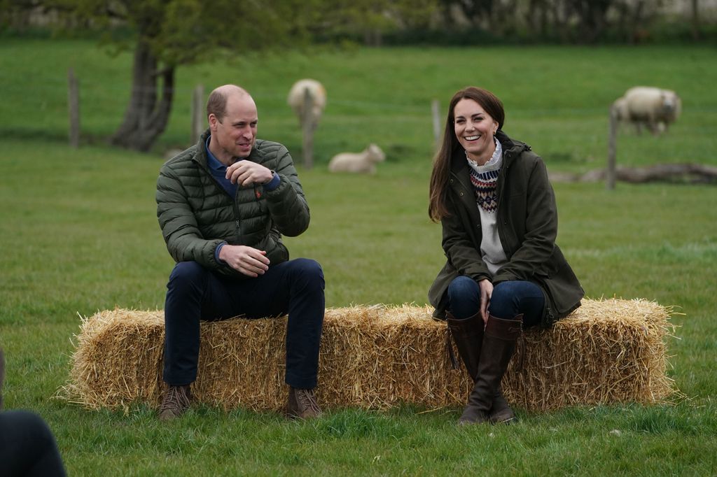 Prince William and Kate Middleton sat on a hay bale with sheep behind them