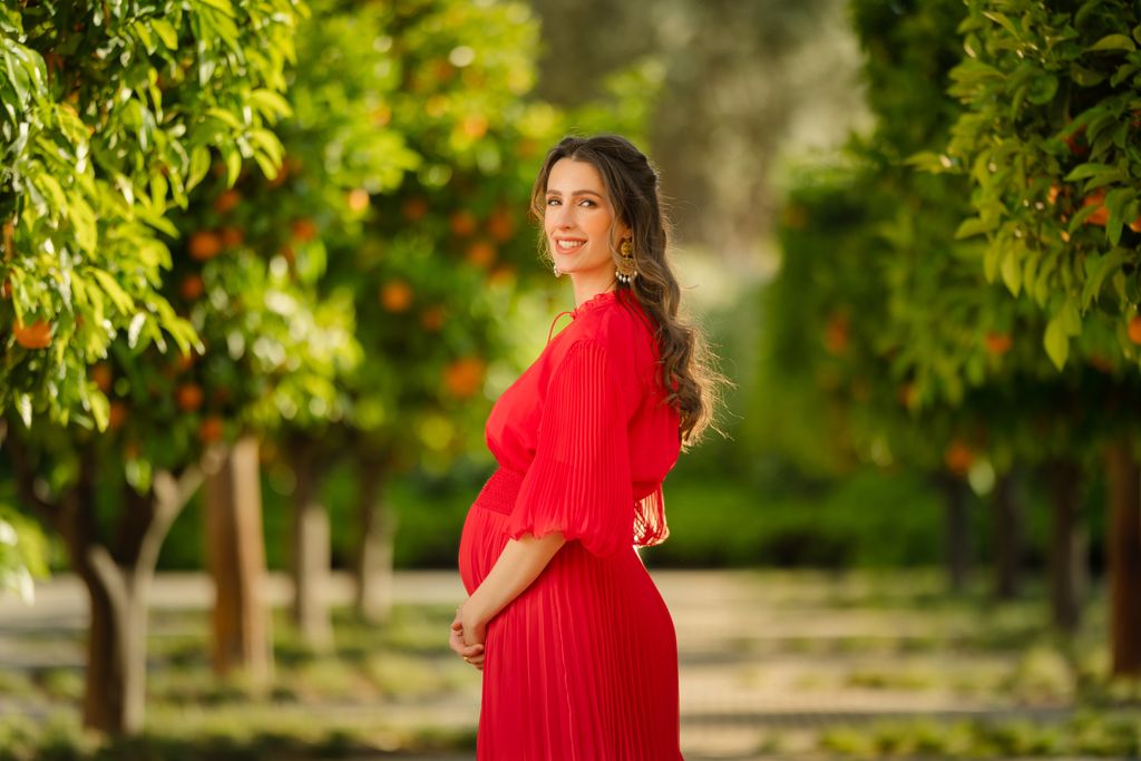 Princess Rajwa standing in an orchard cradling her baby bump