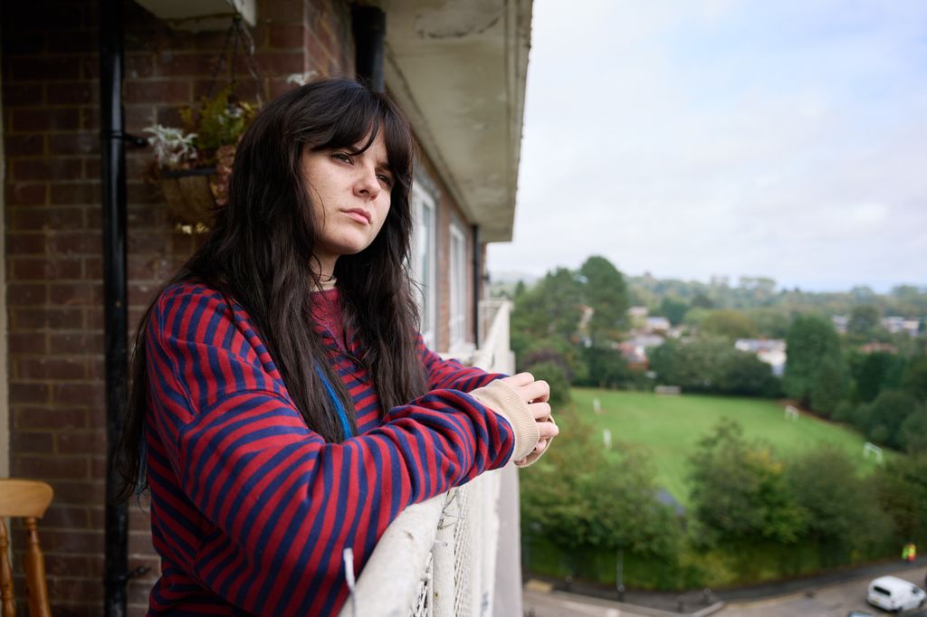 A woman stands on a balcony looking out