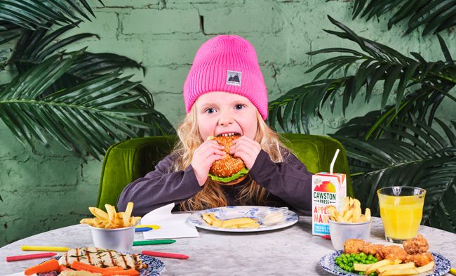 a child tucks into a burger and is surrounded with more food