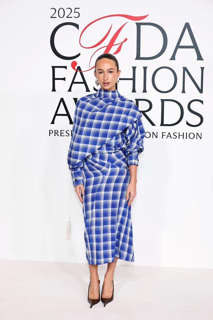 Isabelle Allain attends the 2025 CFDA Awards at The American Museum of Natural History wearing a draped blue checked midi dress with heels
