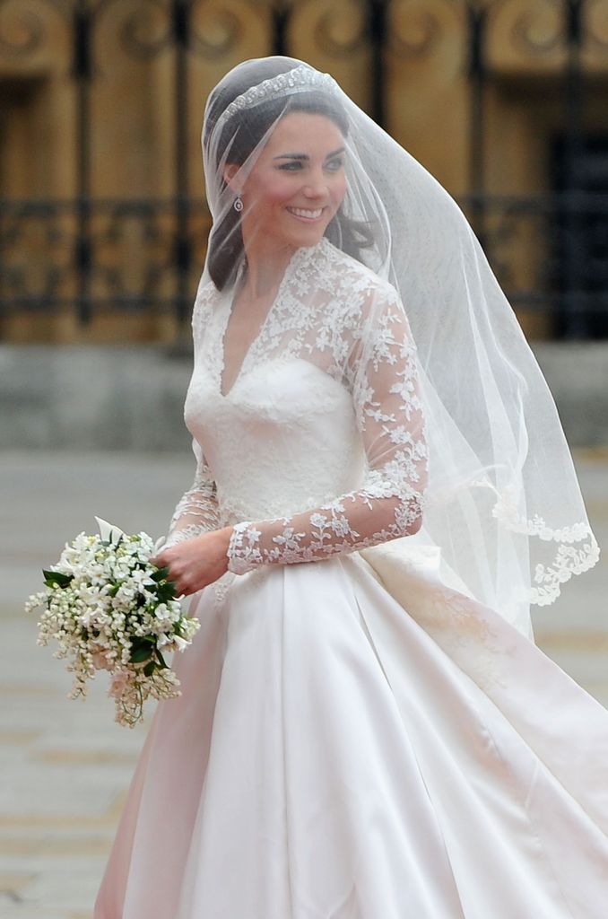 Kate Middleton wearing a veil and a wedding dress looking over her shoulders