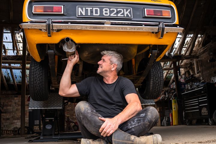 Ant Anstead in black t-shirt pictured beneath a yellow car