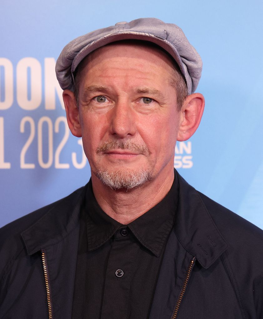 Ian Hart wearing a black jacket and a baker boy hat 