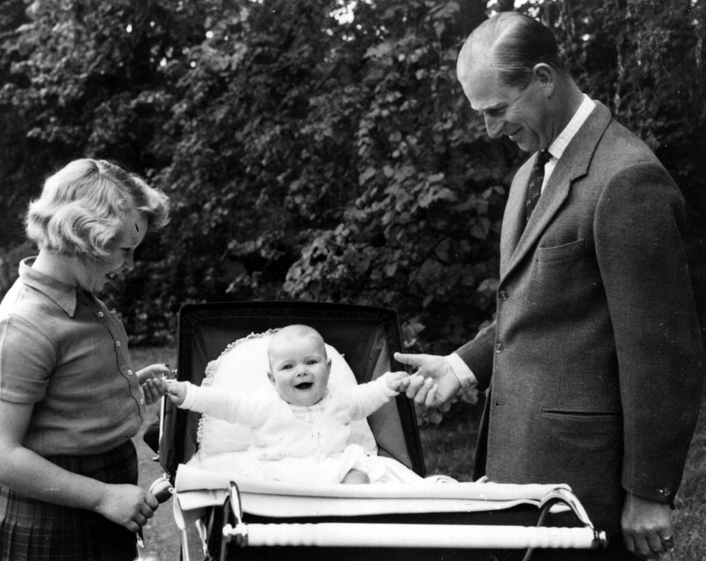 Princess Anne and Prince Philip holding the hands of a baby Prince Andrew