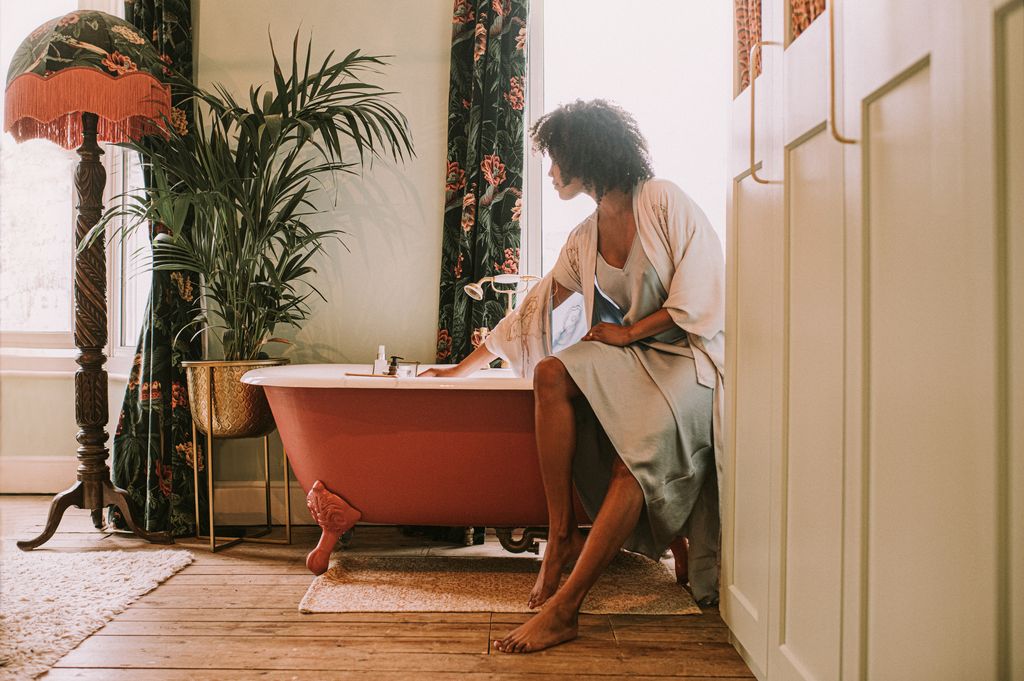 A woman perches on the side of an elegant red roll top bathtub.
