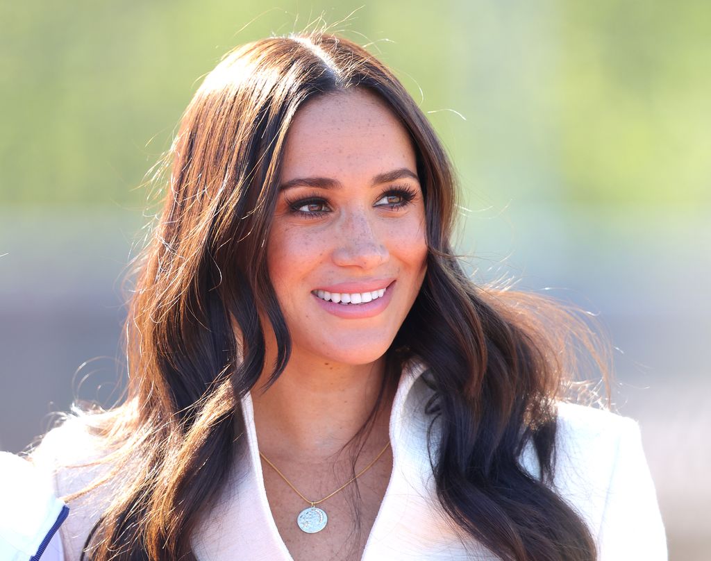 Meghan Markle smiling and wearing a white blazer