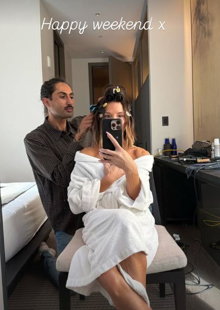 Victoria Beckham posing in a dressing gown while a man works on her hair