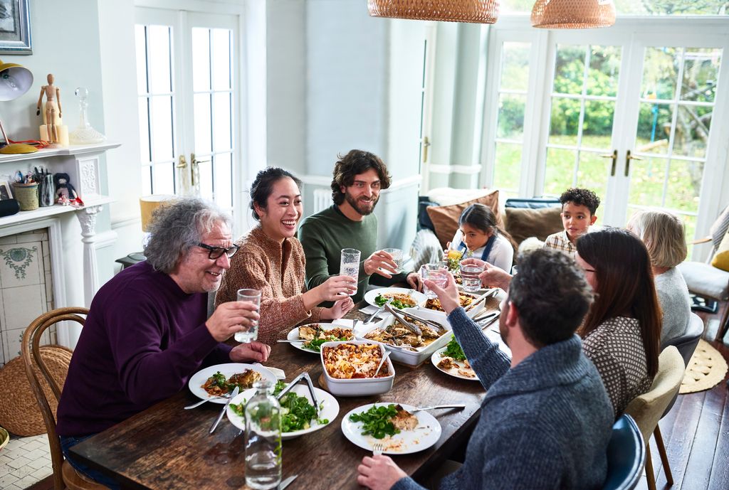 Group of mixed aged relatives toasting drinks at dining table enjoying home cooked meal talking and relaxing, celebration, healthy eating, meal time, domestic life