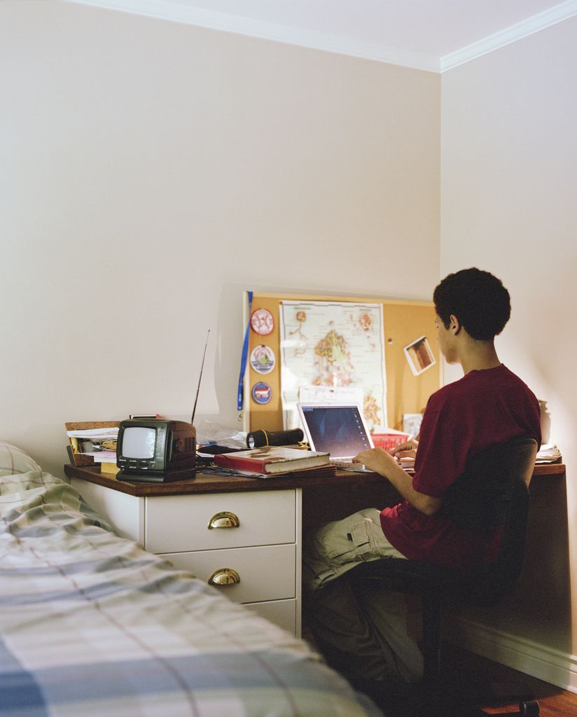 Teenage boy (16-18) using laptop at desk in bedroom, rear view