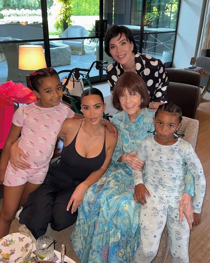 Kim Kardashian posing with her mother, grandmother and two children, wearing a black bodysuit and cargo trousers.