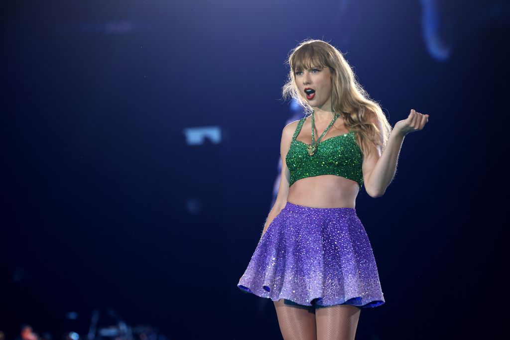 Taylor Swift on stage in a green top and purple skirt looking shocked