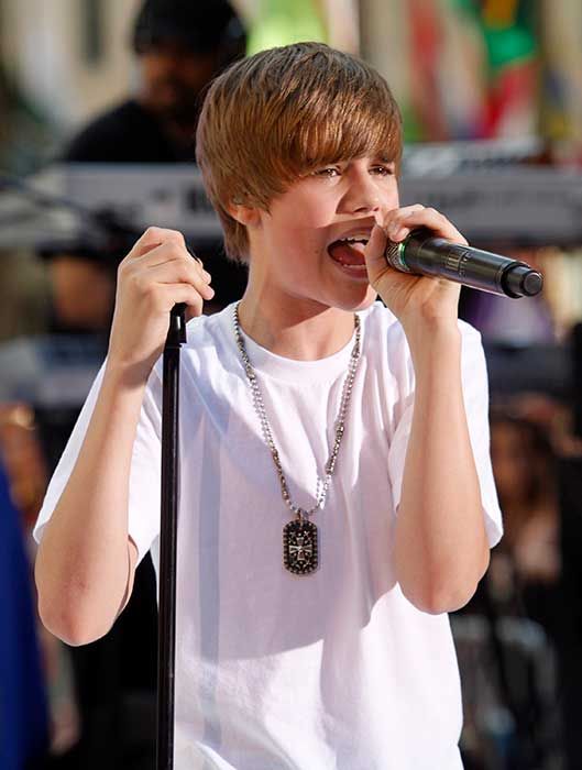A young Justin Bieber singing into a microphone on stage outside