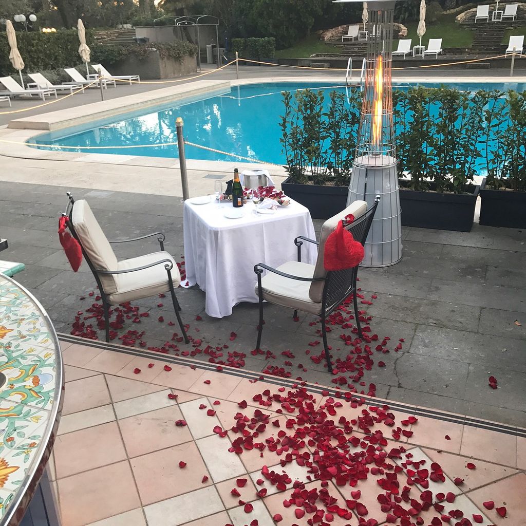 two chairs and a table draped in red rose petals next to a hotel swimming pool and terrace