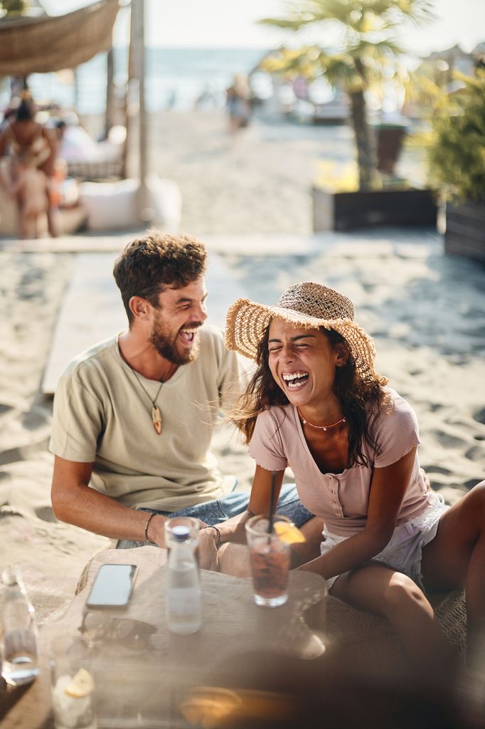 Young cheerful couple talking about something funny while spending a summer day in a beach cafe