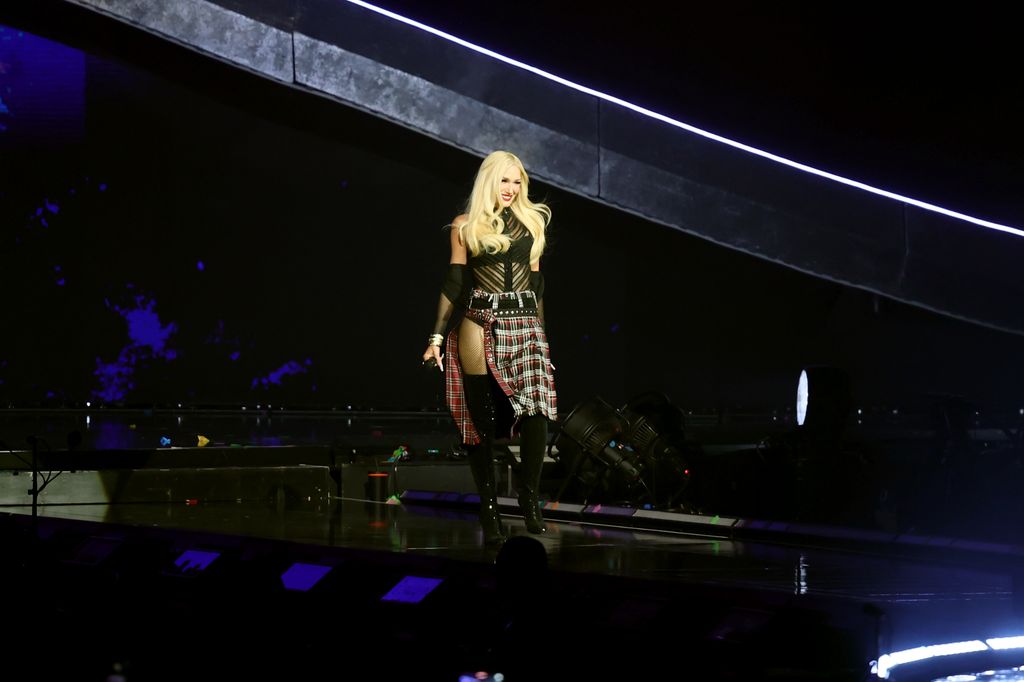 Gwen on stage dressed in sheer top, tartan skirt with thigh-high boots