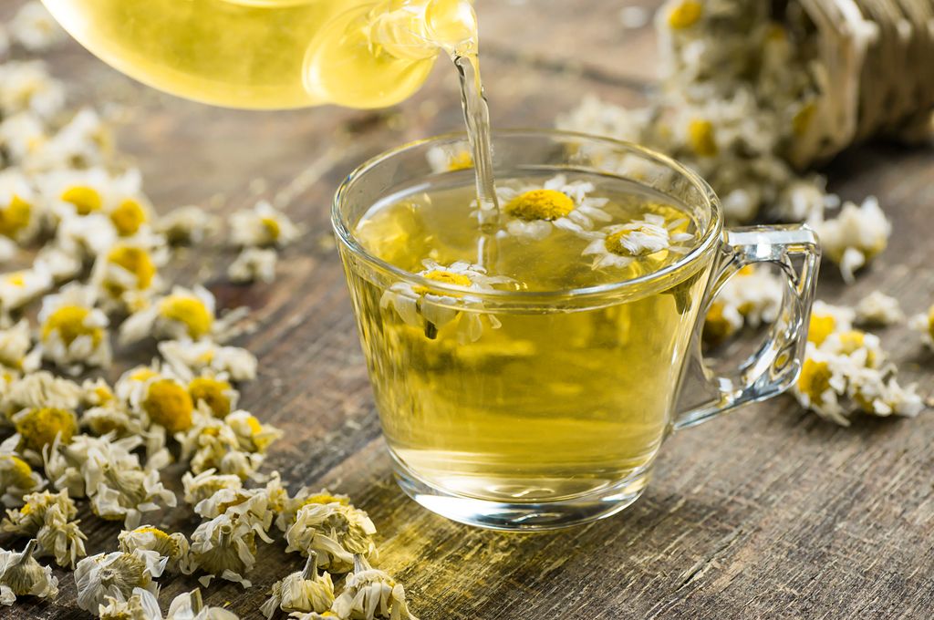 glass cup of chamomile tea with dry daisy flowers and teapot on rustic wooden background