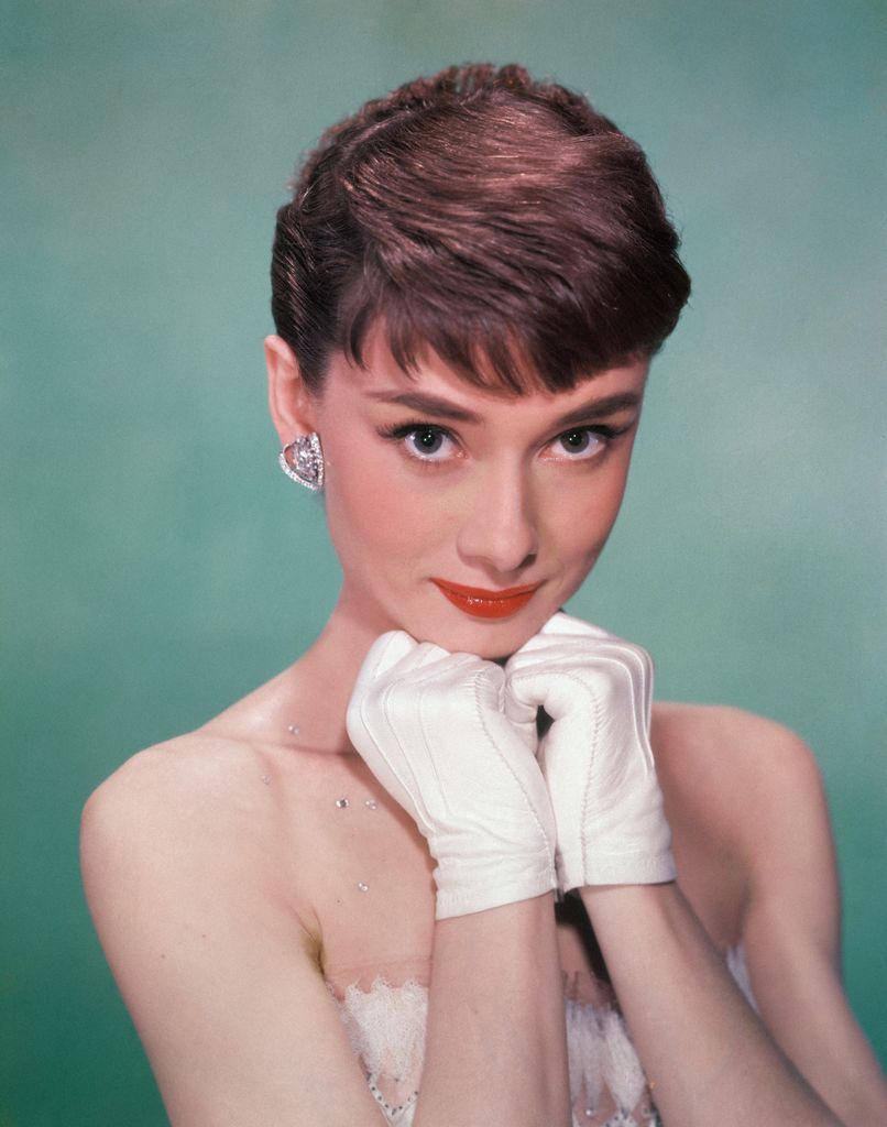 Portrait of Belgian-born American actress Audrey Hepburn (1929 - 1993) as she wears a strapless gown and holds white kid-gloved hands up to her chin
