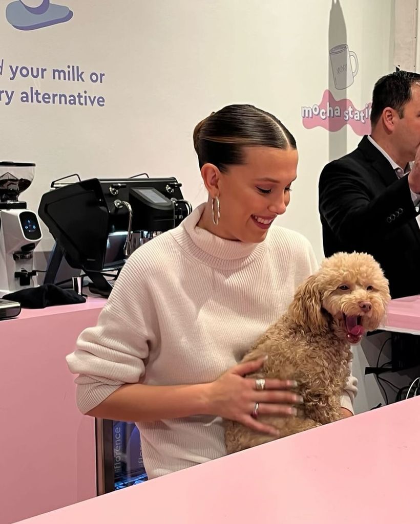 Millie Bobby Brown sitting with a small fluffy dog on her lap