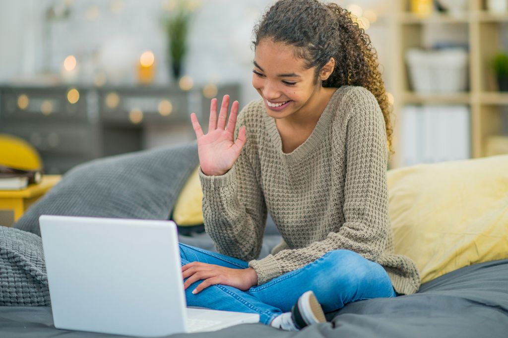 A teenage girl waves goodbye to her friend at the end of a video call.