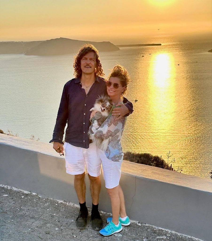 Shania Twain holds her dog Sapphie while posing with her husband Frederic Nicolas Thiebaud in front of the sunset