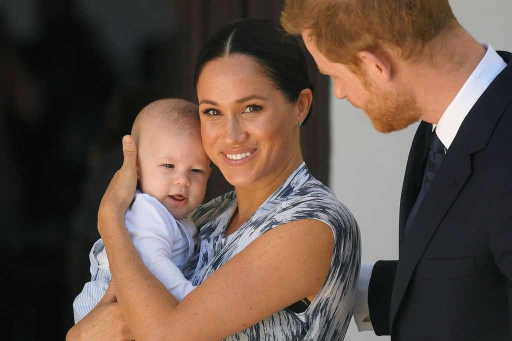 meghan carrying baby archie and prince harry looking on