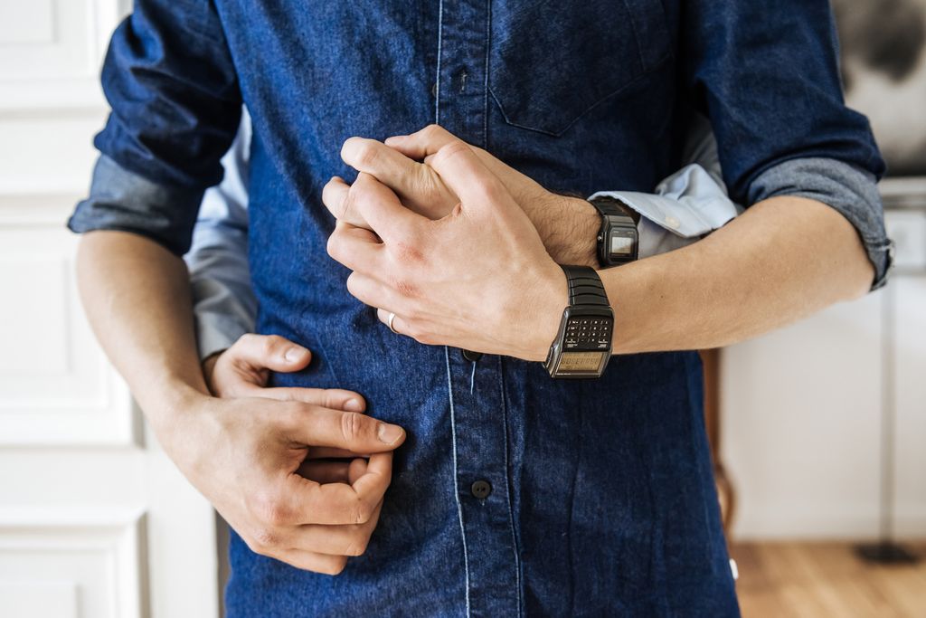 Close up shot of hands of a gay couple hugging. Focus on their hands in front of their body.