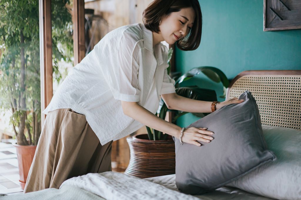 Young woman arranging pillows and making up her bed at home