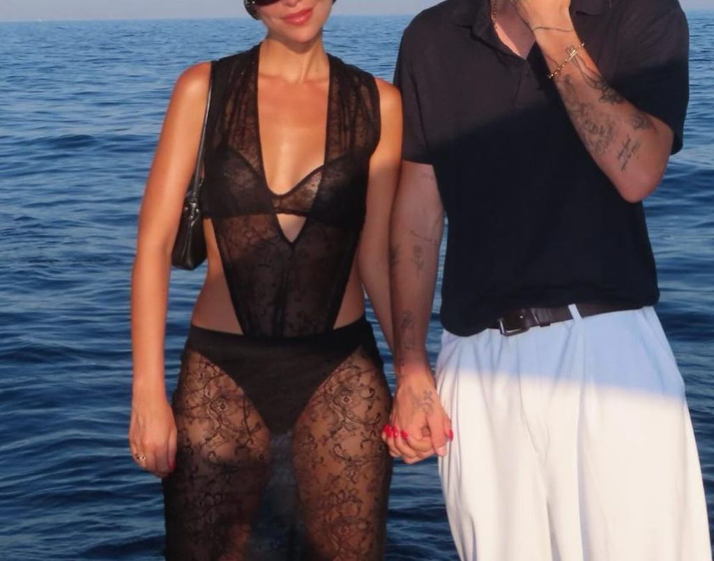 a couple with their heads out of shot hold hands in front of the sea 