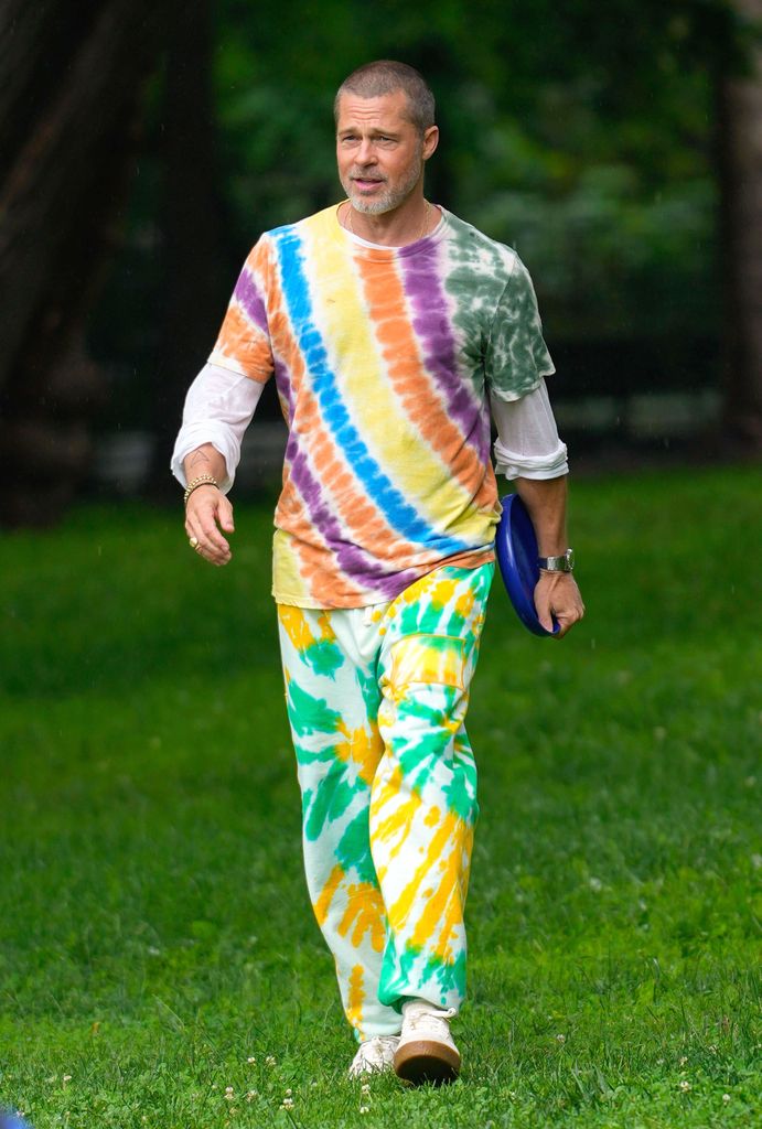 Brad Pitt wears a clashing tie die tshirt and trousers and holds a frisbee in a park