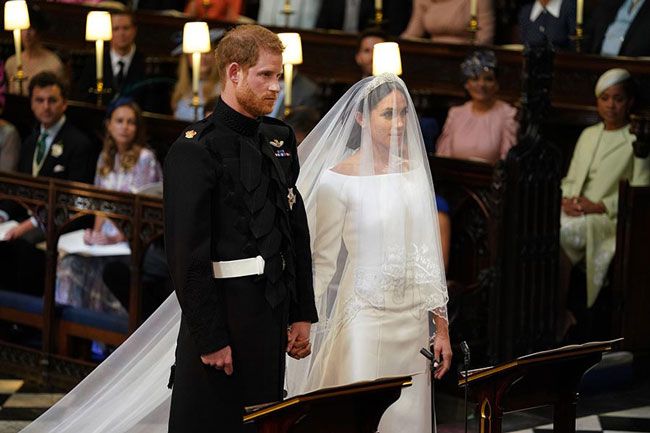 harry wearing military uniform and meghan wearing a wedding dress and veil as they stand at an alter getting married