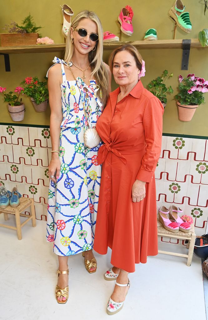 Vogue Williams and Penelope Chilvers attend Chelsea Flower Show 2025 — Vogue William in a colourful print sundress, Penelope Chilvers in a rust-orange shirtdress, both wearing espadrilles and standing in front of floral décor.