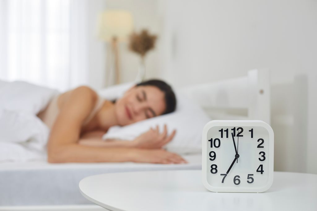 woman lying in bed with table and alarm clock 