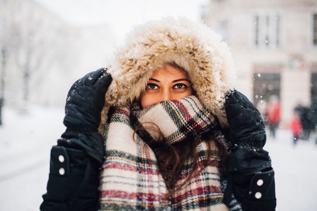 Woman in snowy winter wrapped in a furry hood and a tartan scarf 